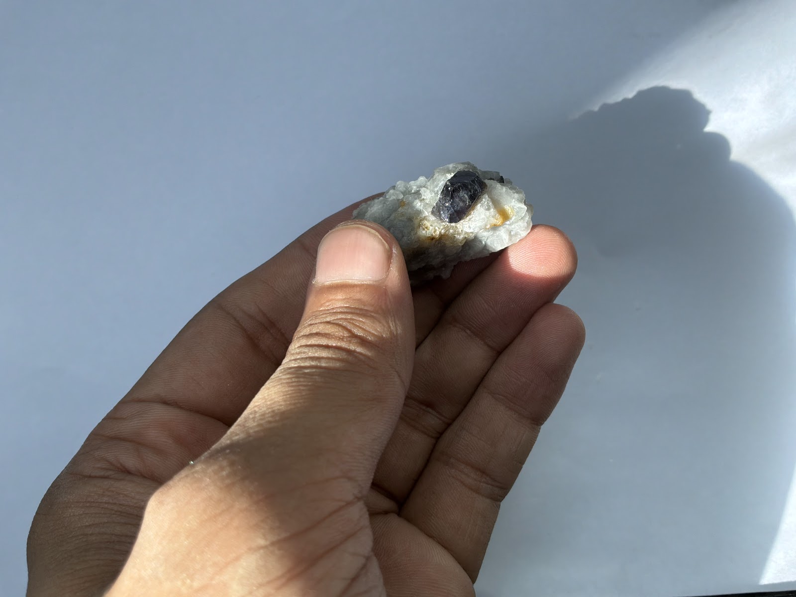 A small piece of pale marble held between finger and thumb, a dark blue-violet corundum crystal set into its upper face