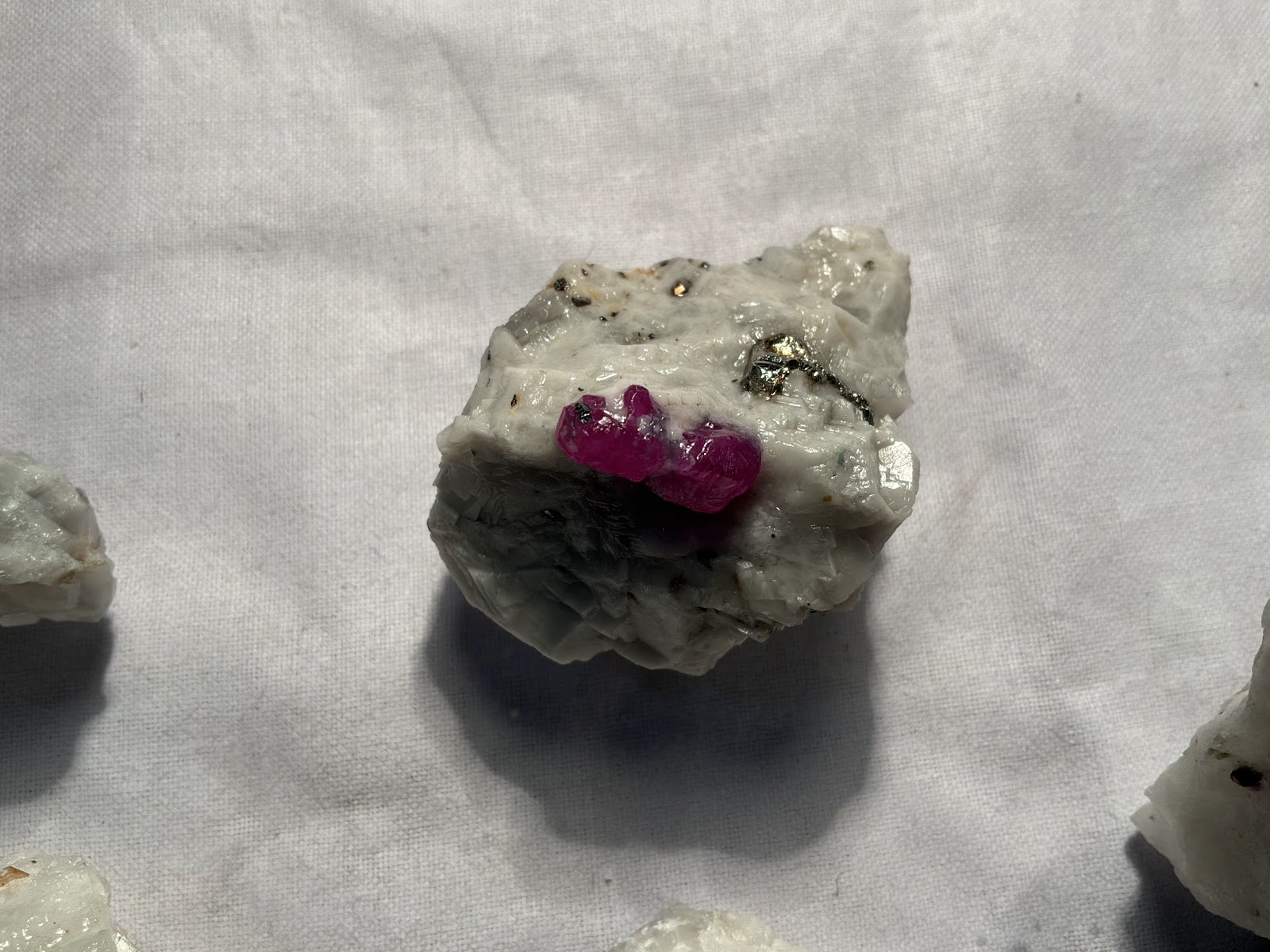 The same ruby and marble piece photographed from a second angle, the pyrite grains and dark mica flecks visible from this side as well