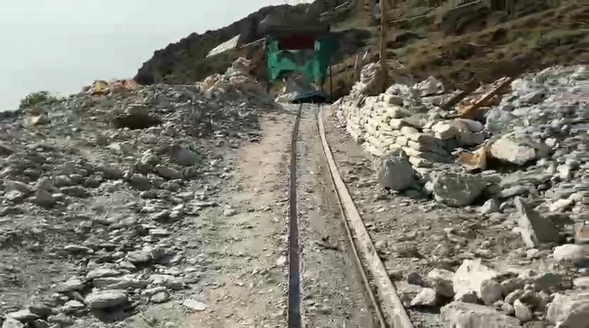 Narrow-gauge rail track running up a slope of boulders towards a green ore chute