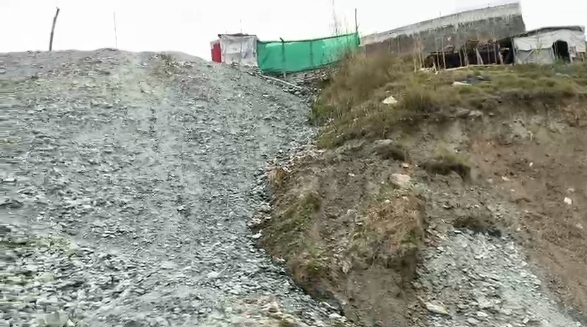 A long slope of grey waste rock below corrugated site buildings on a ridge